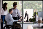 2 Woman 1 man in wheelchair working at desk_1400x800